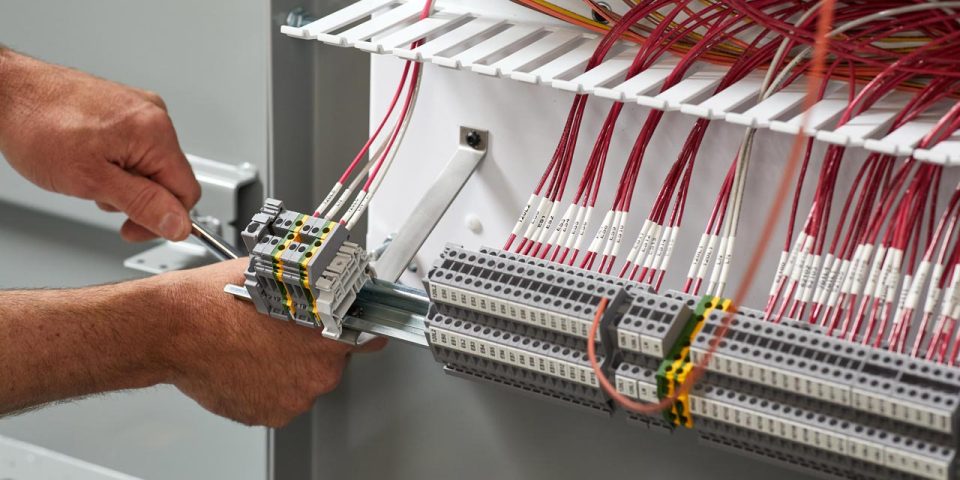 Pair of hands using a tool to adjust a section of a control panel