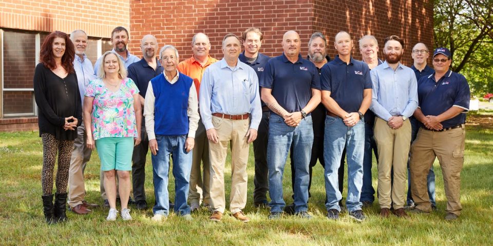 The team members of R.A. Moore pose for a group photograph outside of a red brick building