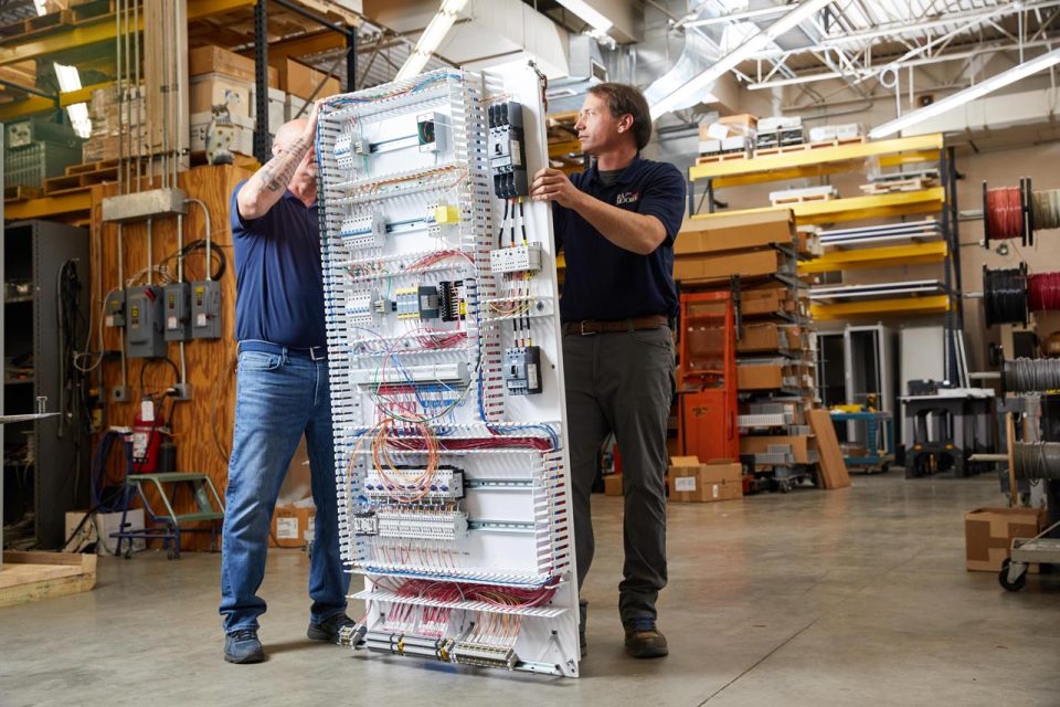 Two employees of R.A.Moore holding a UL certified control panel