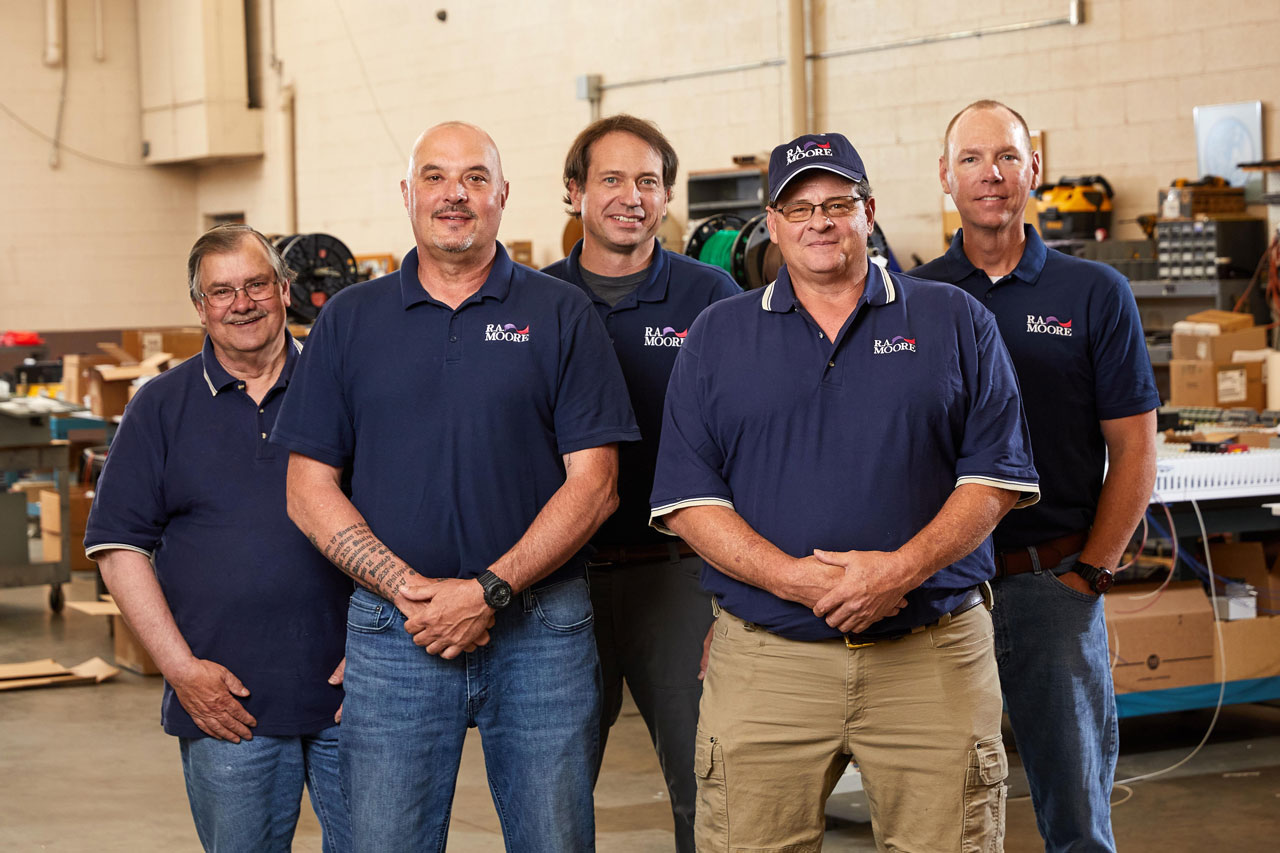 Four employees from R.A. Moore standing together in the warehouse smiling at the camera