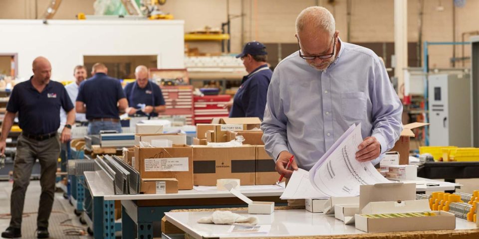 Leadership team member reviewing panel schematics while other employees work behind him in the warehouse