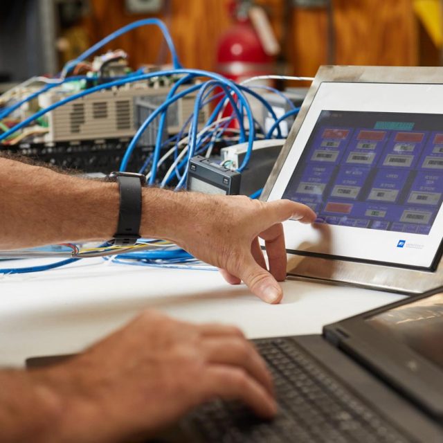 A hand with extending index finger about to select an item from the touch screen of a process control unit