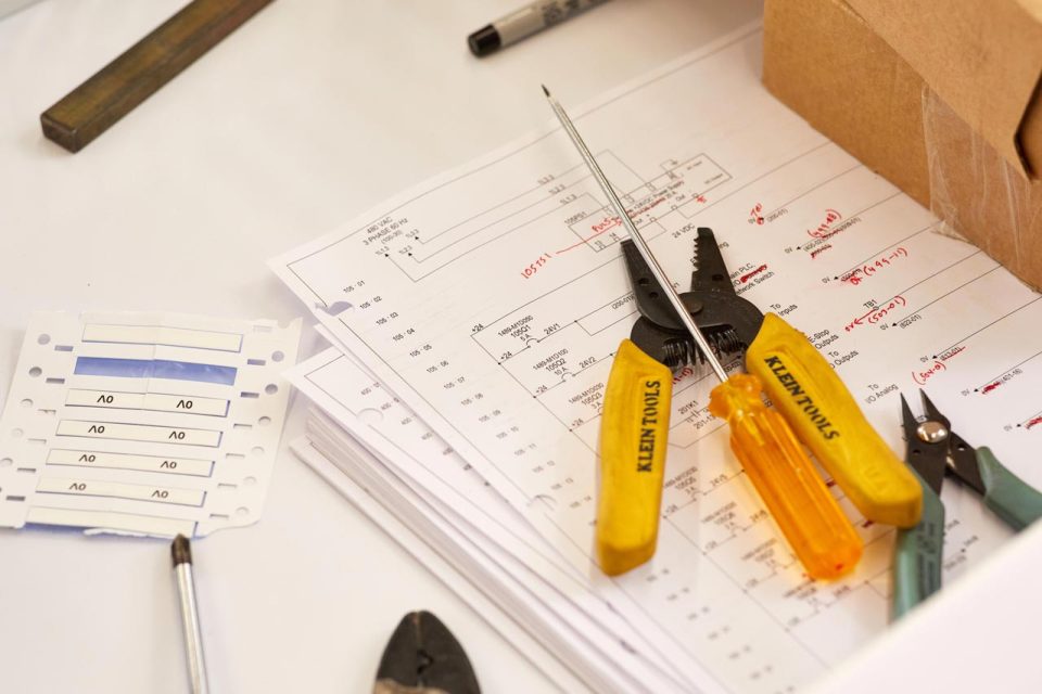 A pair of pliers, a wire cutter, and screwdriver on a stack of papers with red ink markings